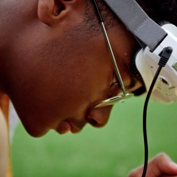 Yusuf, a Black teenage boy, wears a drone headset as he focuses on the controller