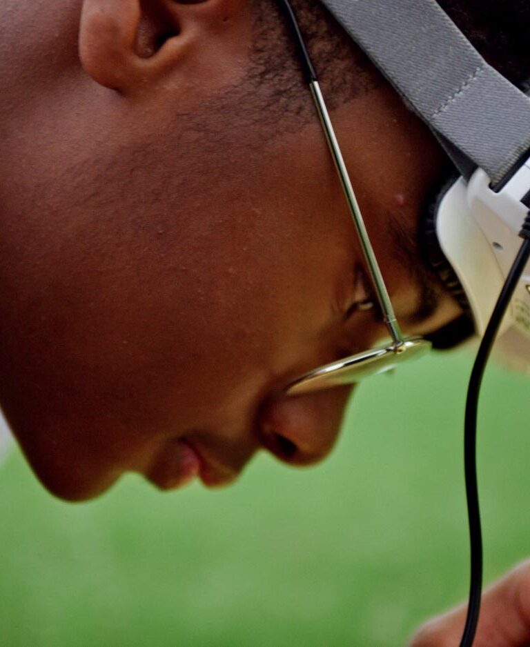 Yusuf, a Black teenage boy, wears a drone headset as he focuses on the controller