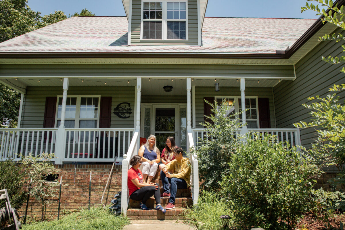 Older mother with three teenage children sharing the steps to the porch of their house