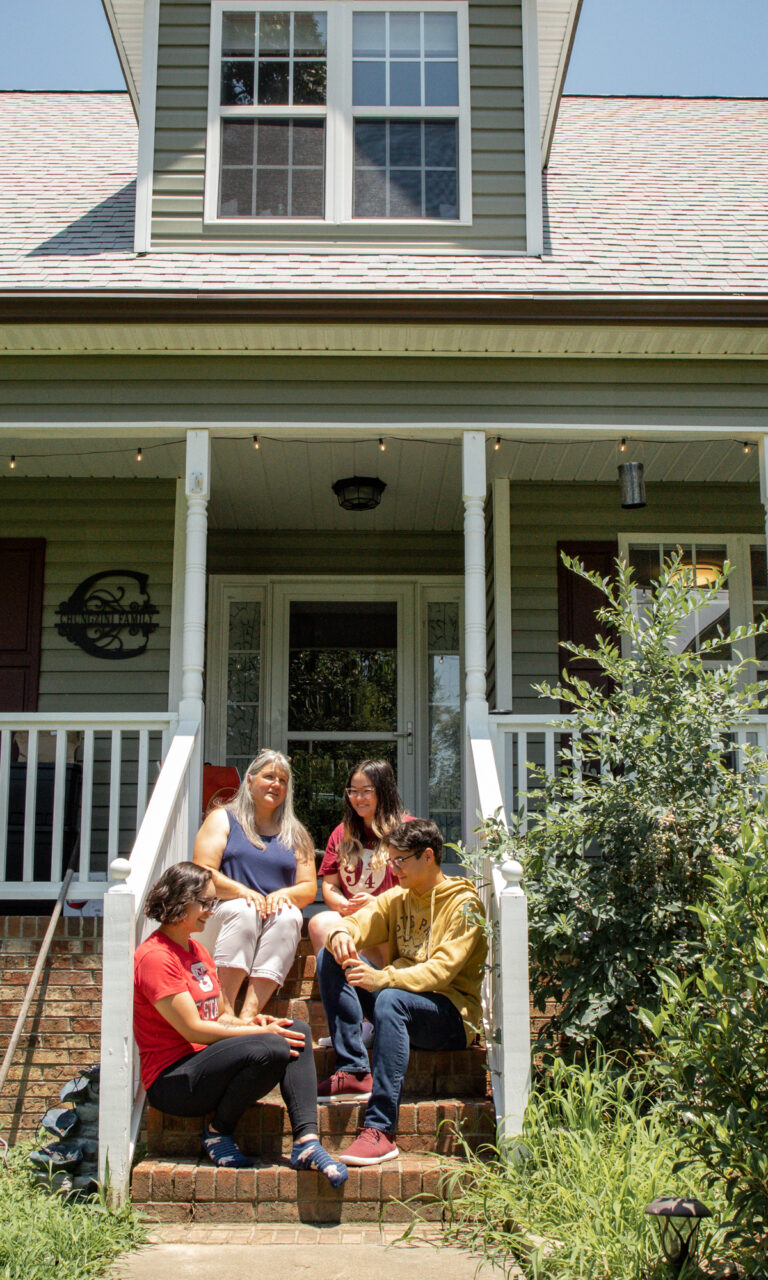 Older mother with three teenage children sharing the steps to the porch of their house
