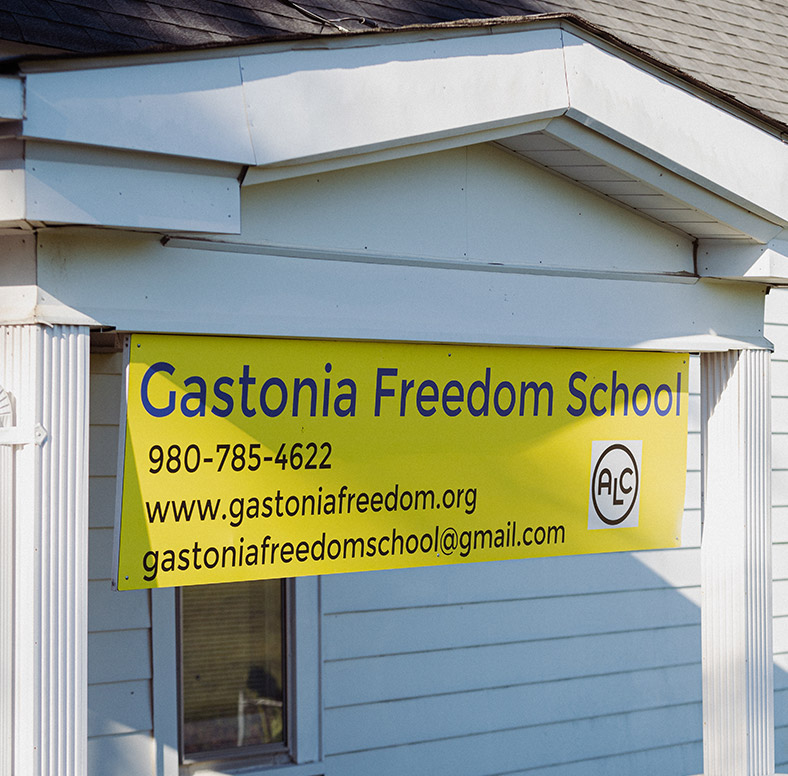 A sign hanging over a small building. Sign says "Gastonia Freedom School. 980-758-4622. www.gastoniafreedom.org. gastoniafreedomschool@gmail.com