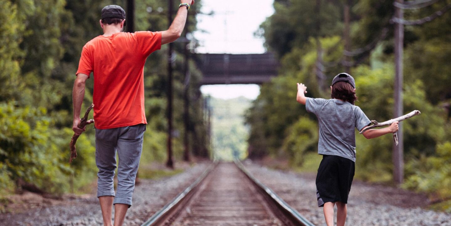 A father and his young son walk together along train tracks