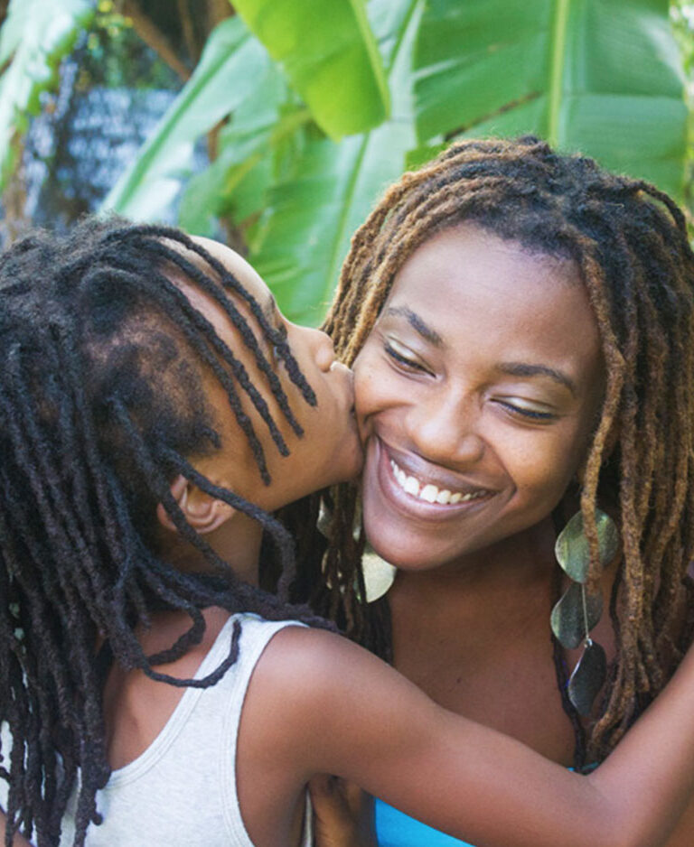 A daughter kissing her mother on the cheek as they embrace in a hug.
