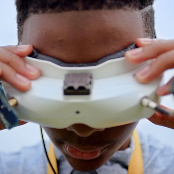 A Black teenage boy looking through VR glasses with his hands on the frame.