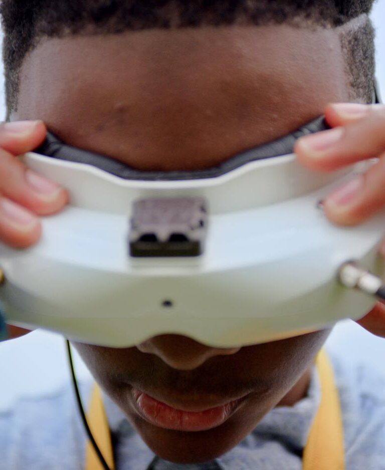 A Black teenage boy looking through VR glasses with his hands on the frame.