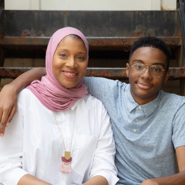 A Black mother in a hijab smiles beside her teenage son