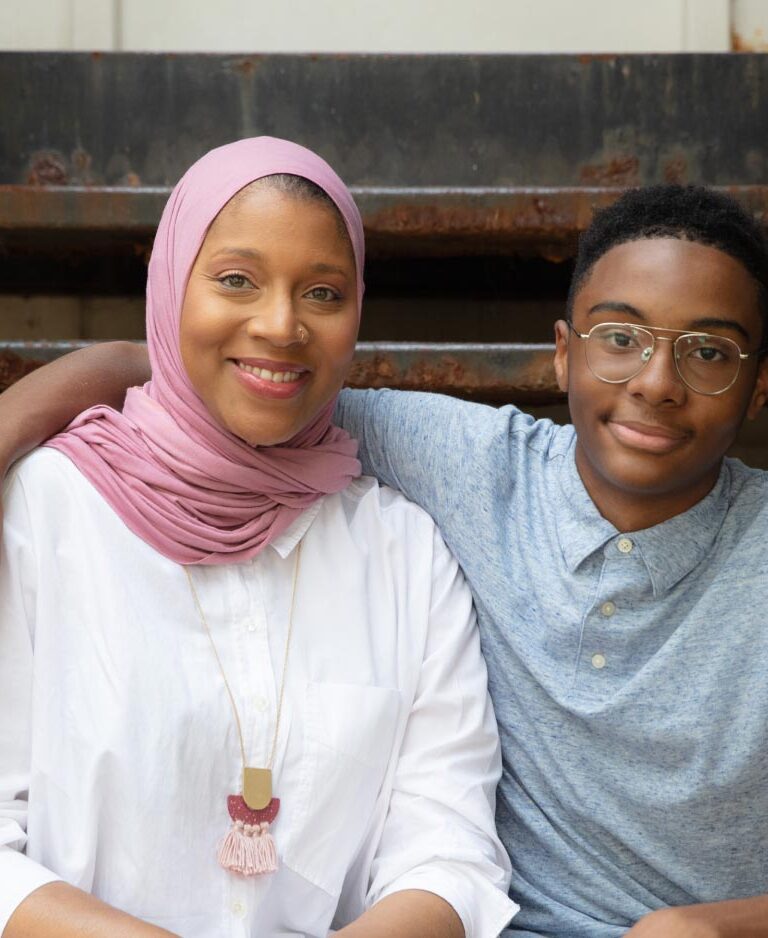 A Black mother in a hijab smiles beside her teenage son