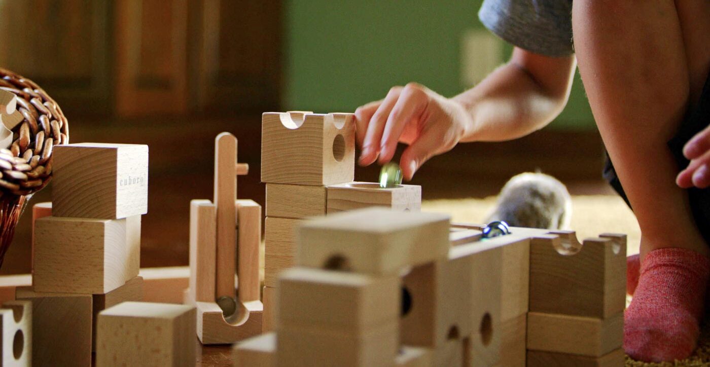 A young boy's hand drops a marble into a stack of building blocks