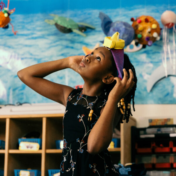 A girl putting on a headband and looking up at the sky while in a classroom.