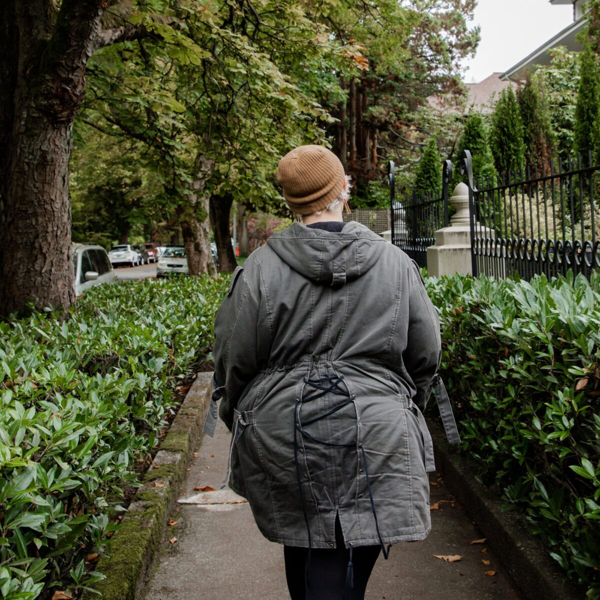 A woman walking on a sidewalk in a trench coat and beanie.
