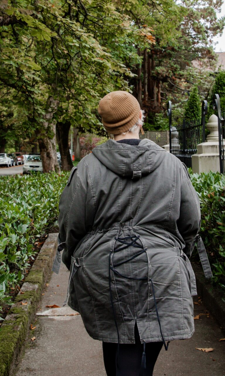 A woman walking on a sidewalk in a trench coat and beanie.