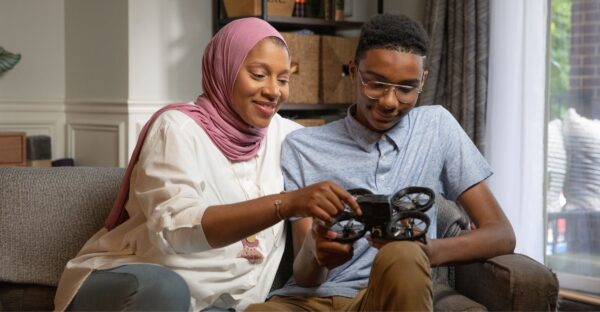 A Black woman in a hijab looks at a small drone with her teenage son